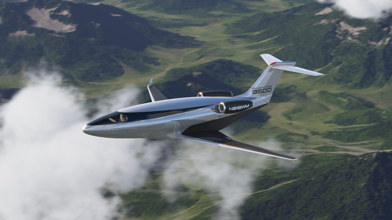 A futuristic-looking render of a silver and black plane above clouds and a rugged landscape