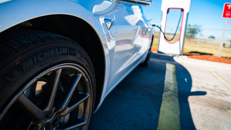 A Michelin tire mounted on a white Tesla Model 3 while supercharging.