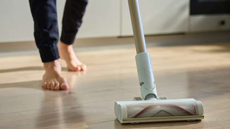 A barefoot person using a stick vacuum on a hardwood floor