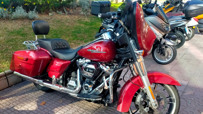A cherry red Street Glide motorcycle parked, showing right side, smaller motorcycles behind