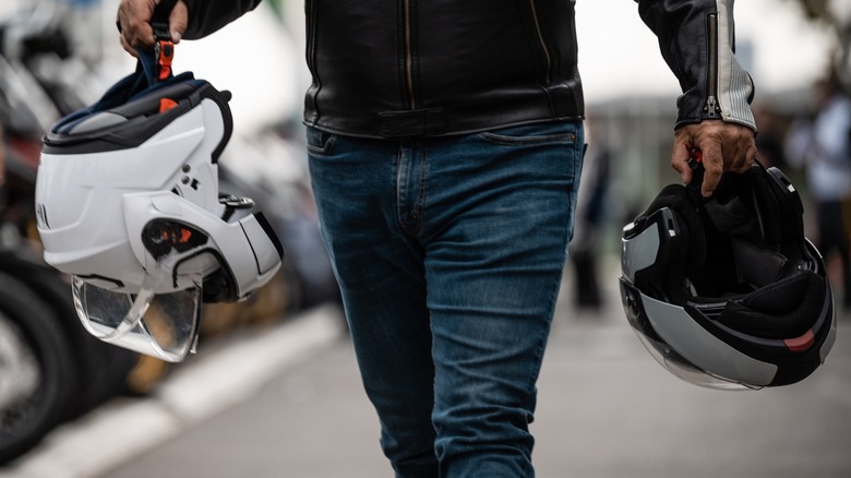 A person carrying a motorcycle helmet in each hand.