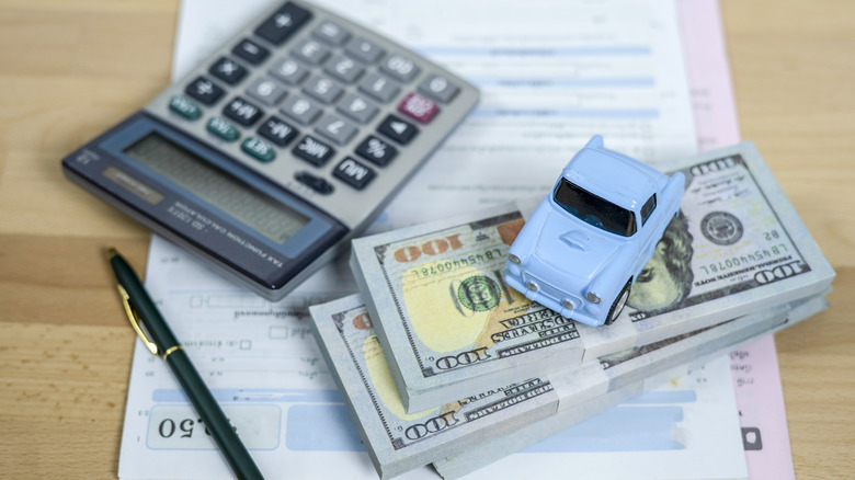 Calculating car expenses with a top car, money notes, and a calculator.