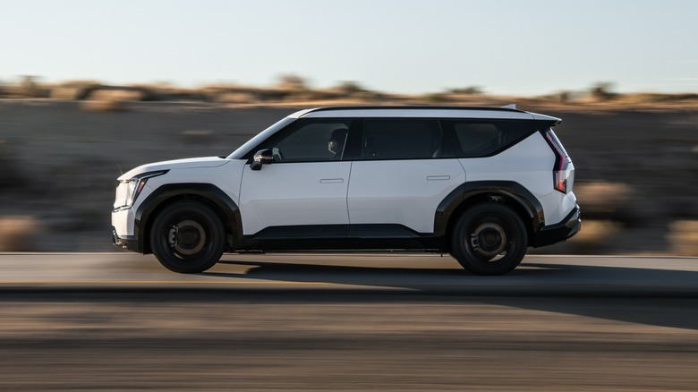 A white Kia EV9 SUV driving at sunset on a rural road