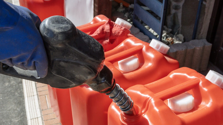 A close-up of a person wearing blue gloves filling up red containers with gasoline.