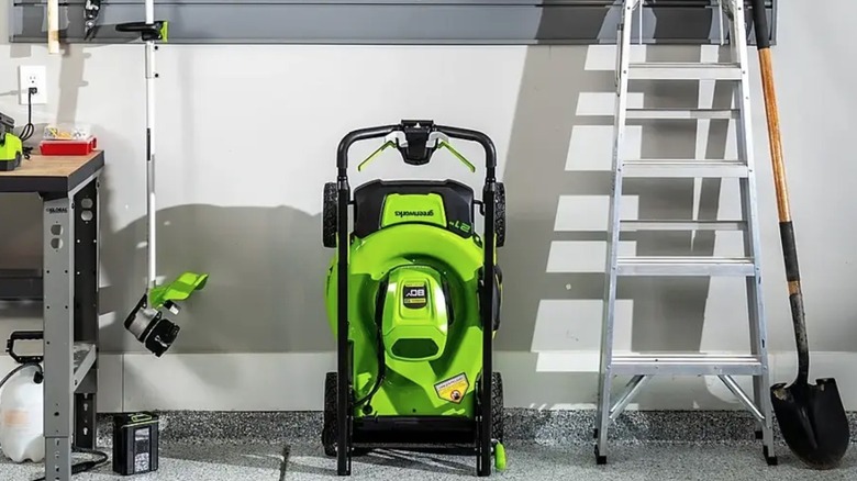 Greenworks lawn mower standing upright while stored away in a garage