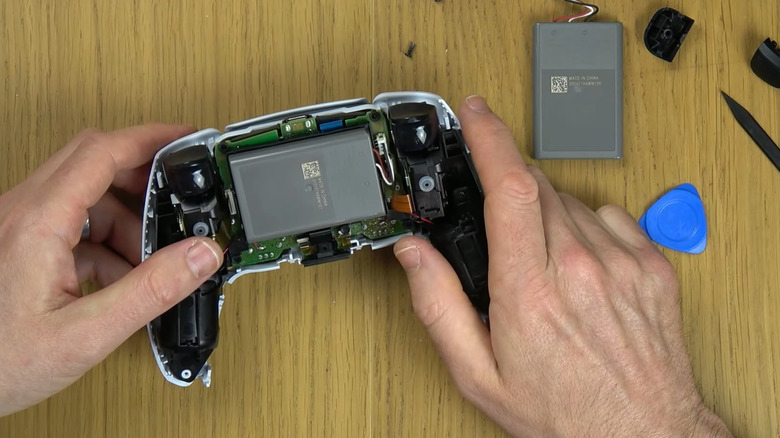 Person holding a dismantled PS5 controller with tools