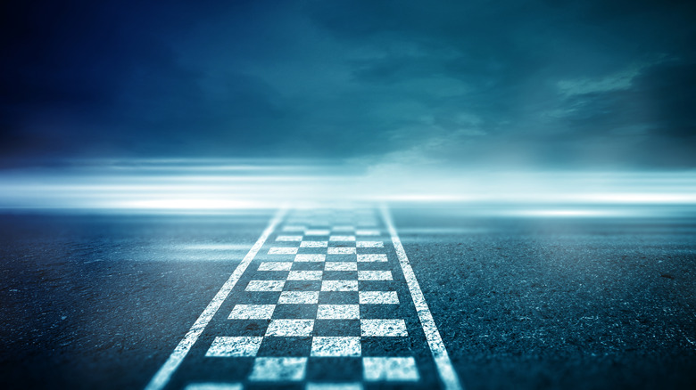 A checkered flag painted on the race track tarmac, blurry lines going across it