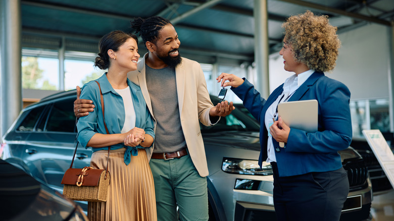 Happy couple receiving car key from dealership salesperson