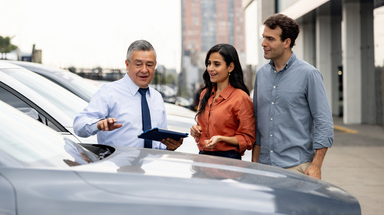 Car salesman showing car to couple outside of dealership