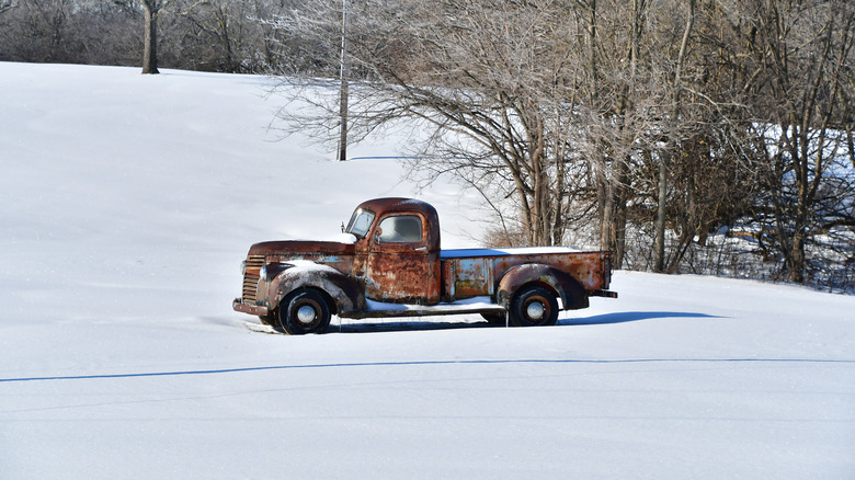 A rusty vintage pickup truck parked in the snow, side view