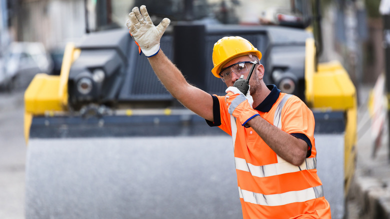 A construction worker in a bright safety vest and hard hat signaling for vehicles to stop