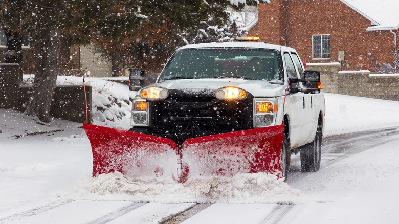A snow plow driving through a residential area.
