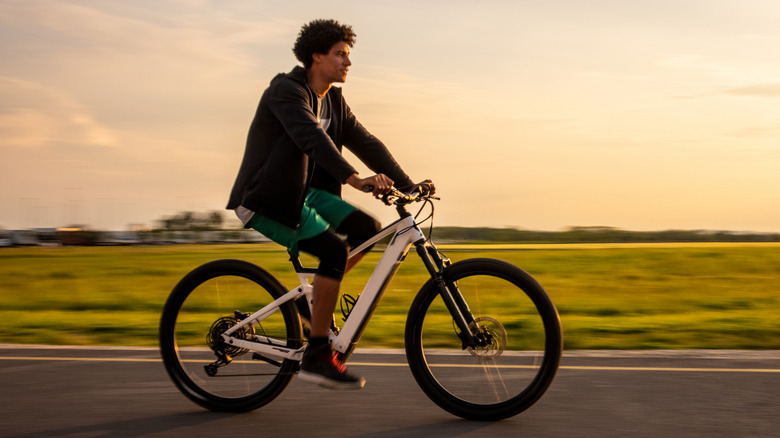 Young man riding electric bicycle on rural road against sky
