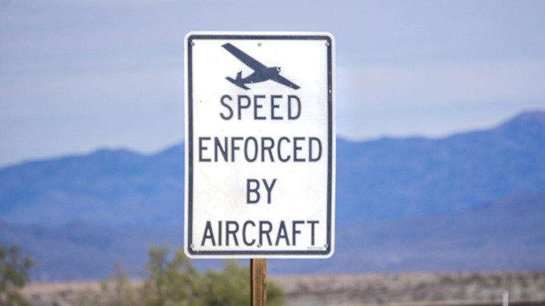 A speed enforced by aircraft sign posted on a road with mountains in the background