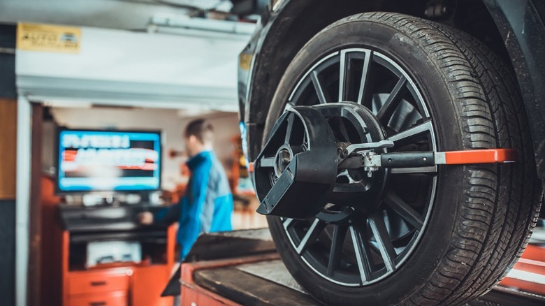 A vehicle on an alignment wrack with sensors installed on the wheels and a mechanic in the background reading the data