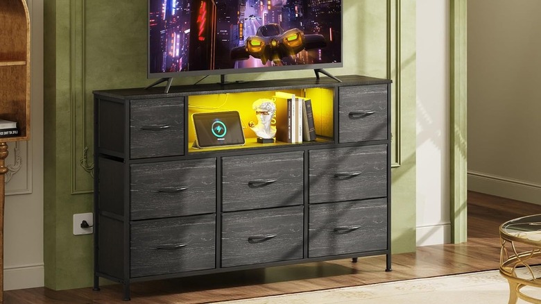 A TV stand that is plugged in with a tablet charging next to some books under a TV.