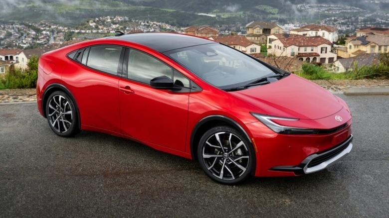 A supersonic red Toyota Prius PHEV XSE parked on the roadside with a cityscape and hills in the background.