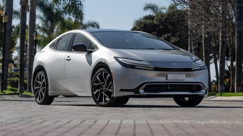 A Cutting Edge 2025 Toyota Prius Plug-in XSE parked on a paved surface with palm trees and other greenery in the background.