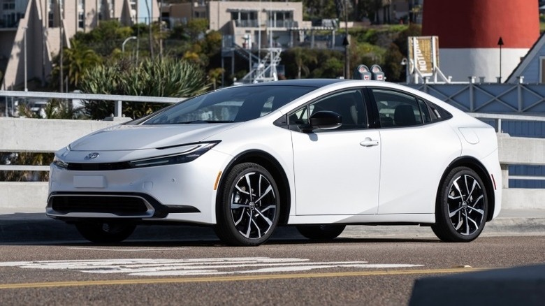A Wind Chill Pearl 2025 Prius PHEV XSE parked on a bridge with buildings in the background.