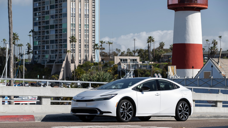 2026 Toyota Prius PHEV driving along coastal road with lighthouse in background, front-left 3/4 view