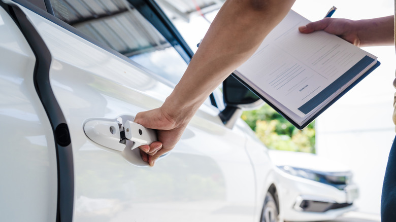 A person holding papers while opening a car door.