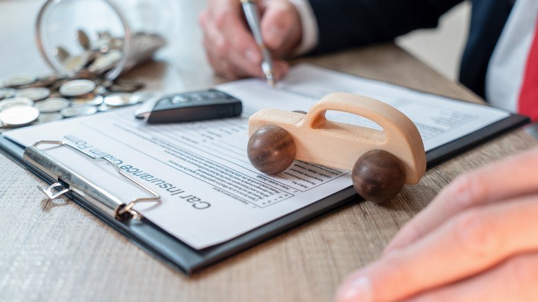 A person writing on auto insurance documents.