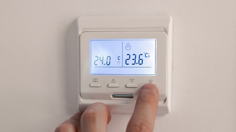 Someone's finger on the thermostat power button poised to turn it off.