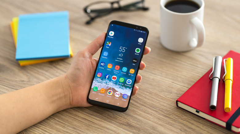 A person holding an Android smartphone over a wooden table