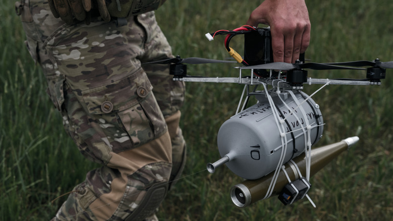 Soldier holds a drone in grassy environment.