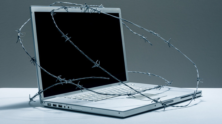 A computer is wrapped in barbed wire, symbolizing  restrictions on its usage.
