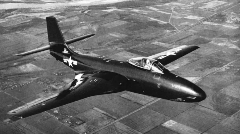An F2H-1 Banshee in flies over cornfields in black and white