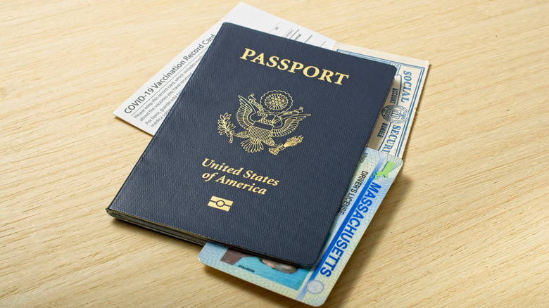 Contemporary Personal Identification Information set of passport Social Security Real ID and COVID-19 Vaccination card all lying on wooden tabletop.