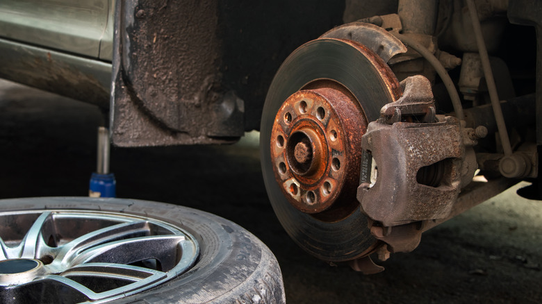 Car wheel removed showing rusty disc caliper and rotor