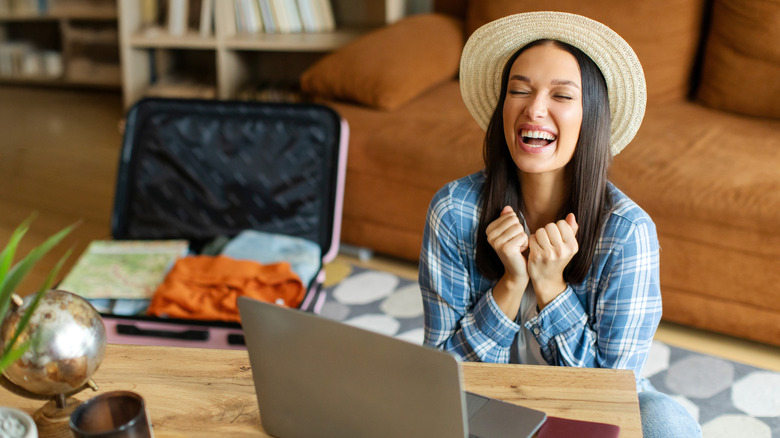 Happy woman with computer open surrounded by travel gear