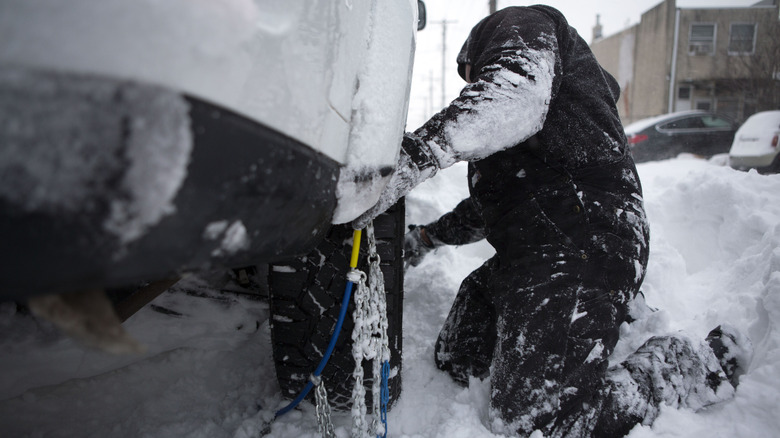 A person intalling tire chains on a car during snowy conditions.