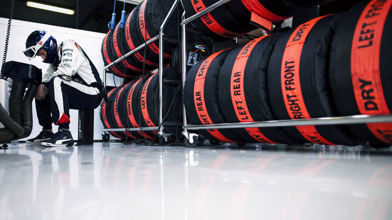 Racks of Formula One tires in blankets in garage with engineer servicing components