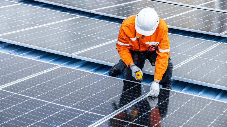 A professional wearing orange jacket installing solar panels on roof