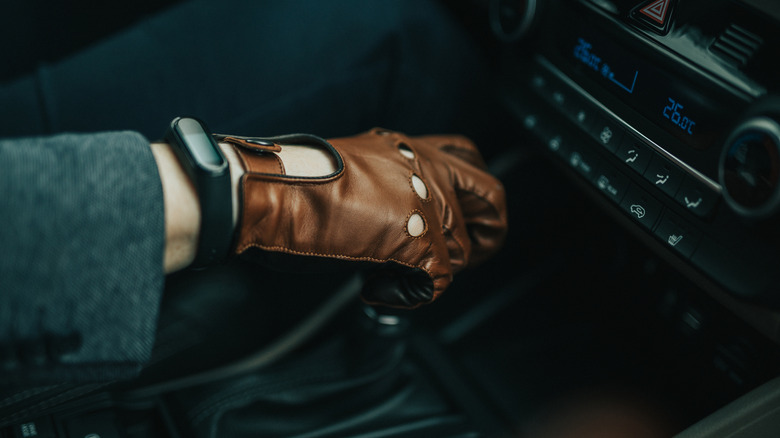 A person wearing driving gloves holding a gearshift.