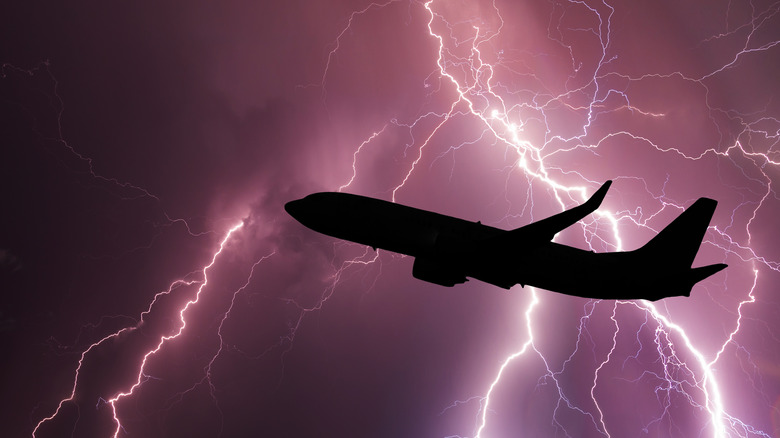 Silhouetted plane flying through lightning