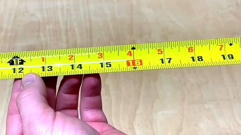 Man holding tape measure blade with bold red numbers