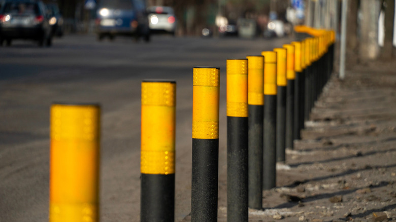 Yellow and black bollards are arranged in a neat row along a city street as cars pass by in the background