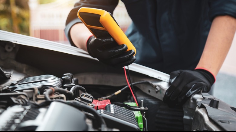 An auto repair technician checks an automobile battery.