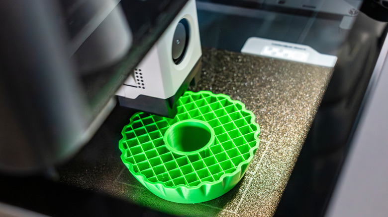 A 3D FDM printer prints a green object using PLA filament.