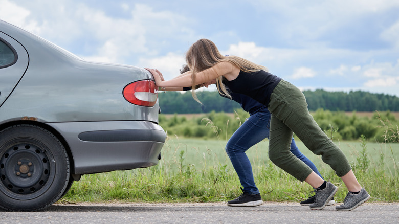 Two people pushing a 90s Renault, side rear view