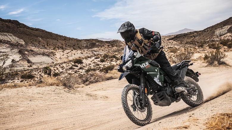 A rider on a dirt trail in the desert on a Kawasaki KLR 650 motorcycle.