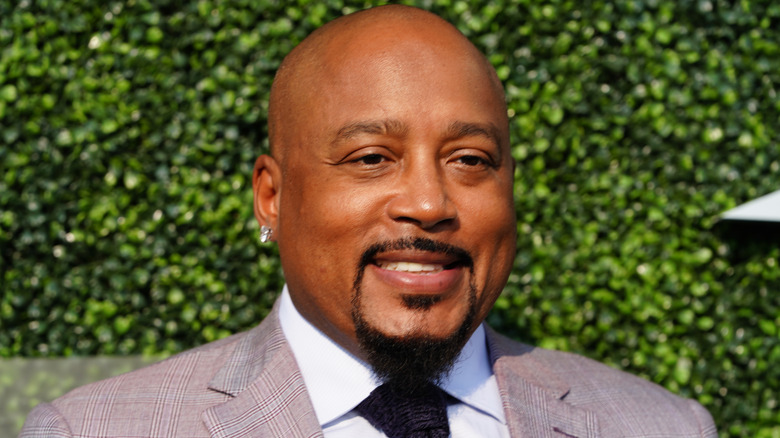 Daymond John smiling  in front of green hedge wall