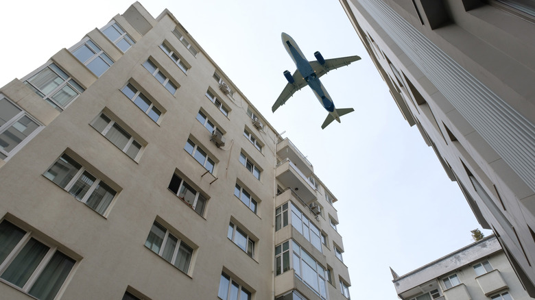 The underside of a flying passenger jet with tall city buildings rising into the air
