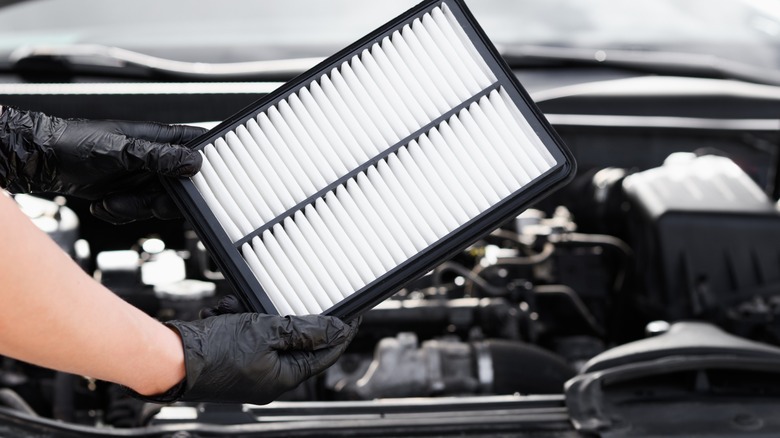 Person holding car engine air filter in fron of car engine