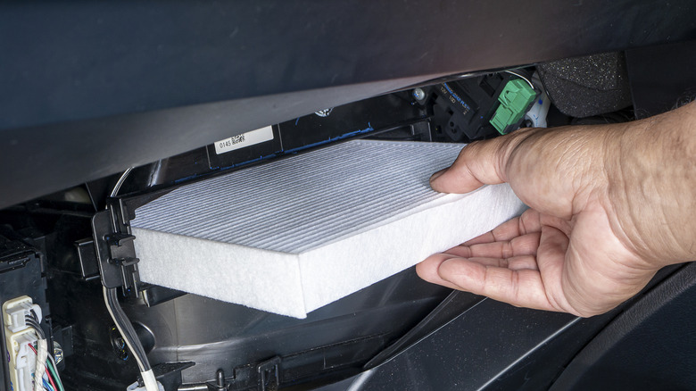 Picture of a cabin air filter being put into its place by a hand