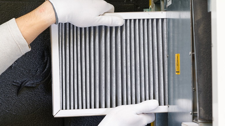 A person with white gloves holding used HVAC filter